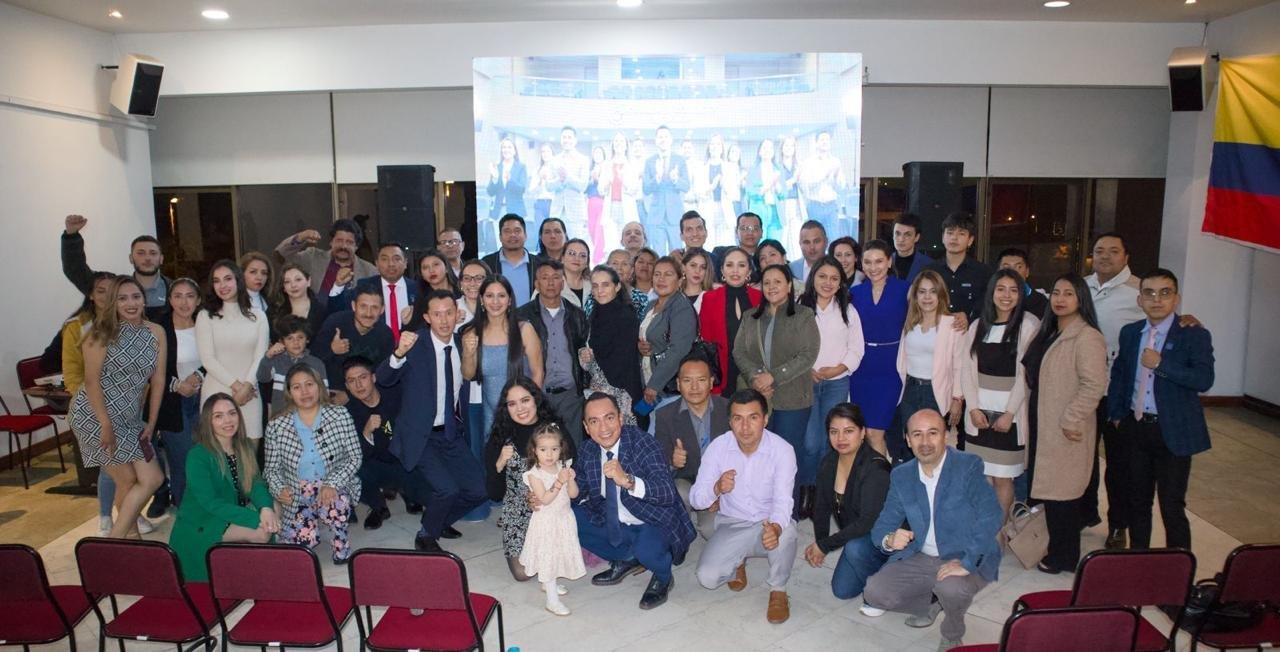 Gran equipo reunido en salón de eventos con pantalla y bandera de Colombia